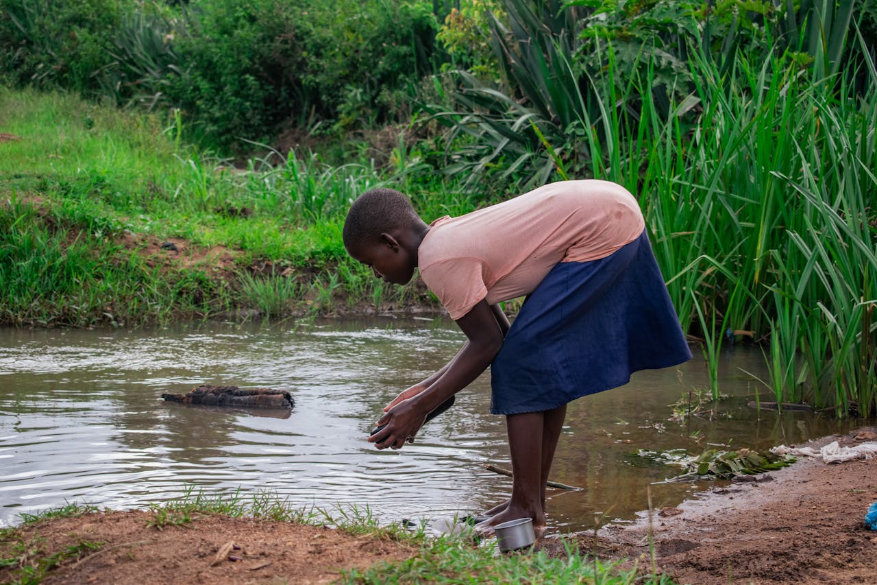 A child gathers water from a rural stream in Dowa, Malawi, amidst lush greenery.