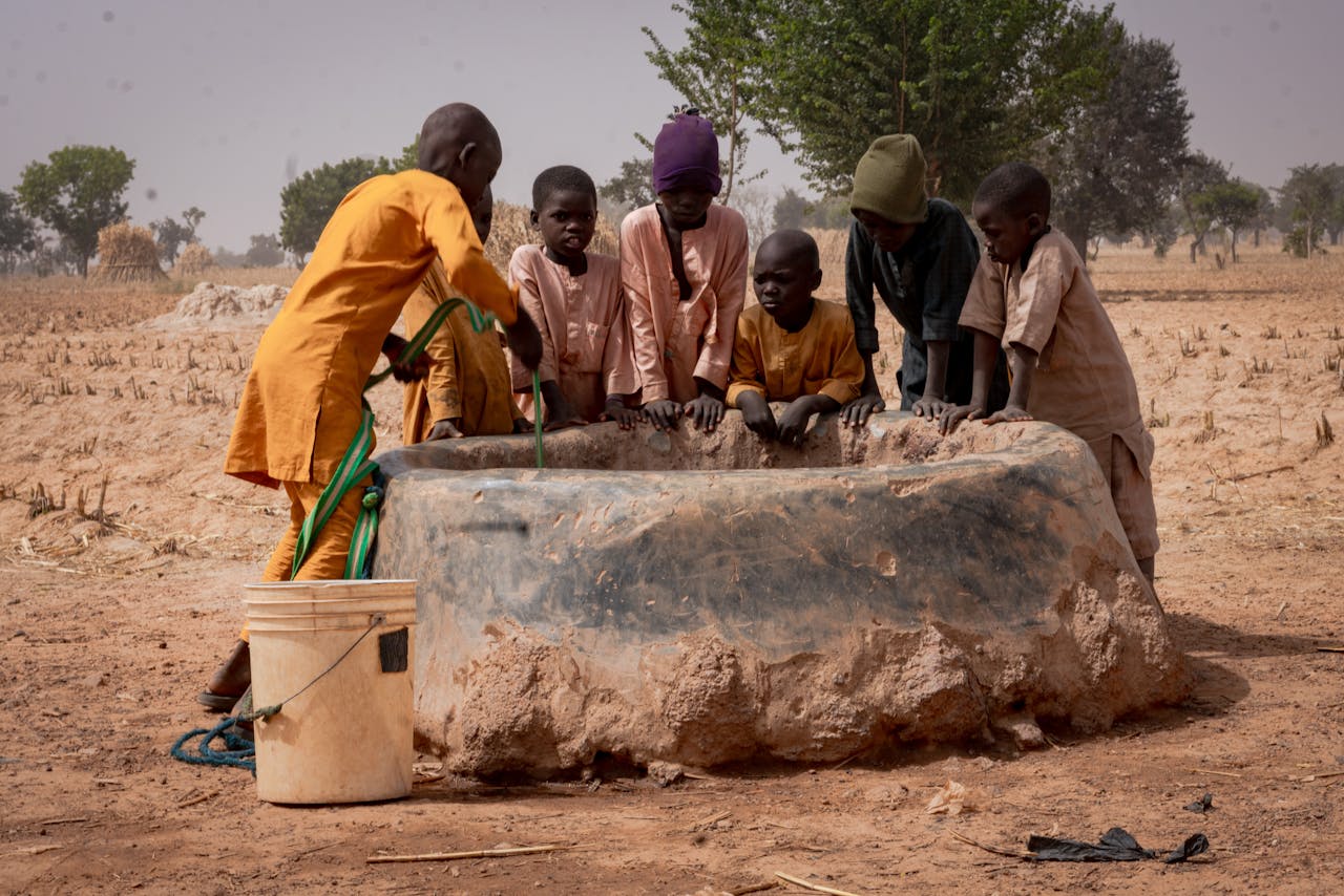 Group of children fetching water from a well in a rural landscape.