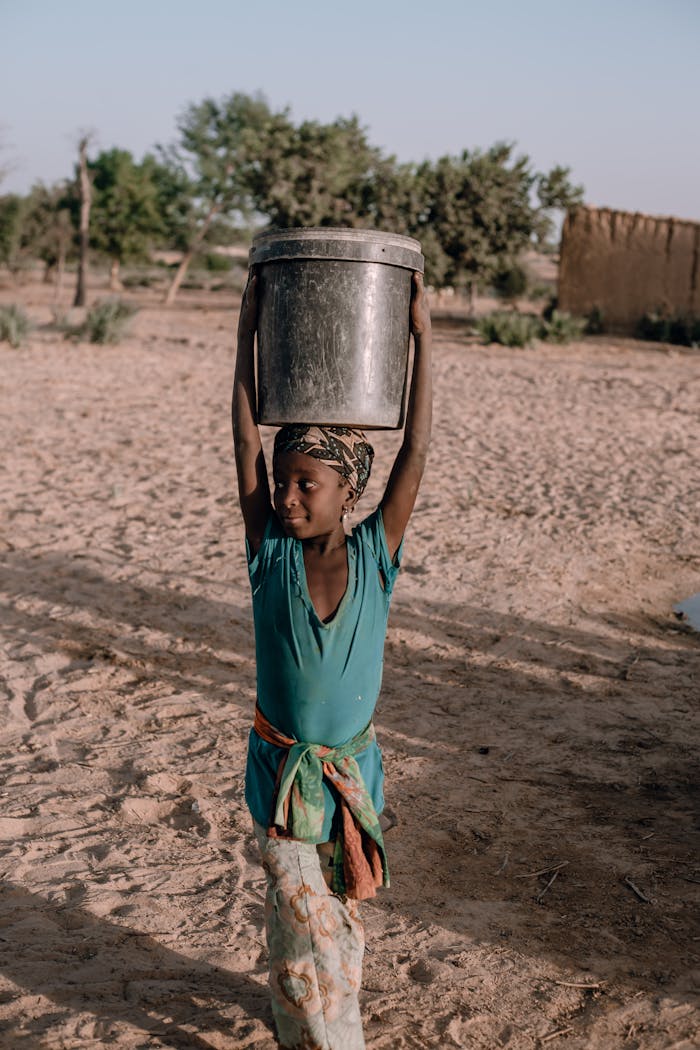 A young girl carries water in a rural Nigerian village, showcasing daily life and resilience.