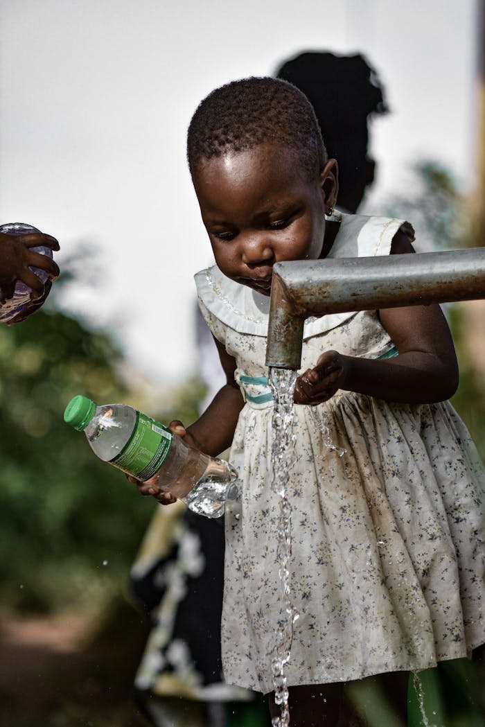 A young girl collects fresh water from a tap in Kampala, Uganda, ensuring water safety.